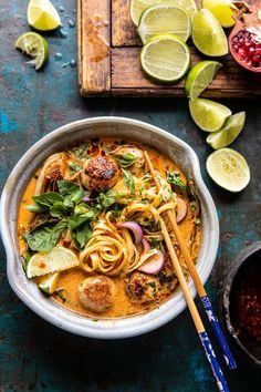 a bowl of thai noodle soup with chopsticks and lime slices on the side