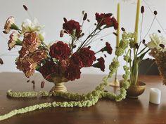 flowers are arranged in vases on a table with green ribbon and candlesticks