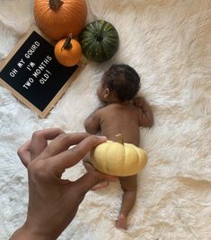 a baby laying on top of a white rug next to pumpkins