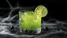 a green drink in a glass with a lime slice on the rim and spider legs around it