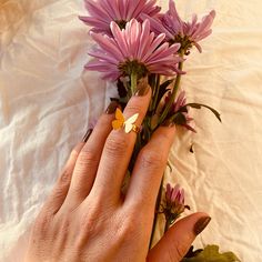 a woman's hand holding some flowers on top of a white bed sheet,