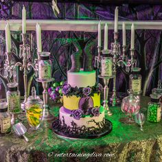 a table topped with a cake covered in purple and green frosting next to candles