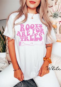 a woman with long blonde hair wearing a white t - shirt that says roots are for trees