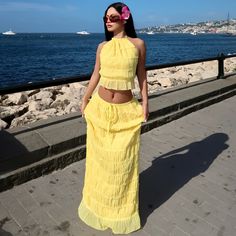 a woman in a yellow dress is standing on the sidewalk near the water and looking off into the distance