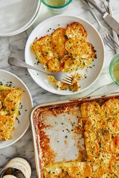 two plates with lasagna casserole on them next to silverware and forks