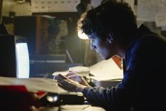 a man sitting at a desk in front of a computer monitor looking at his cell phone