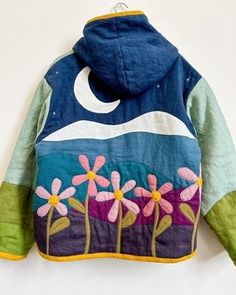 a jacket with flowers painted on it hanging from a hook in front of a white wall