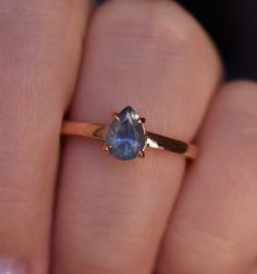 a woman's hand holding a ring with a blue stone on it and gold band