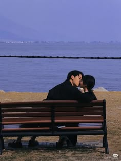 two people are kissing on a bench by the water