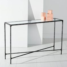 a glass and metal console table with two small vases on the top, in front of a white wall