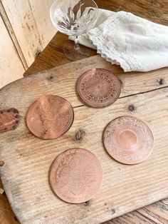 four copper coins sitting on top of a wooden table next to a glass vase and cloth