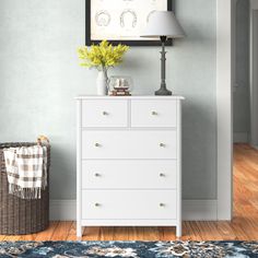 a white dresser sitting next to a lamp on top of a wooden floor