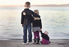 a man, woman and child standing on the beach looking at the water with their arms around each other