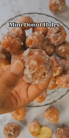 a person holding a doughnut in front of a glass bowl filled with donuts