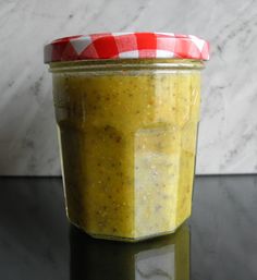 a jar filled with yellow sauce sitting on top of a table next to a marble wall