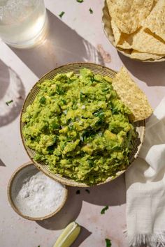 guacamole in a bowl with tortilla chips next to it on a table