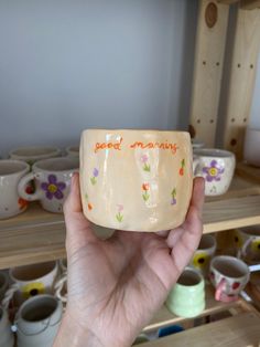 a hand holding up a ceramic cup with the words good morning written in orange on it