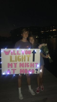 two people are holding a sign that says will you light my night at hog?