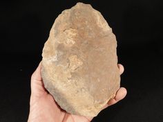 a hand holding a large rock on a black background in front of a person's hand