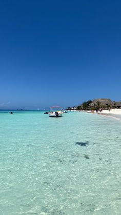 a boat floating on top of a body of water next to a sandy beach under a blue sky