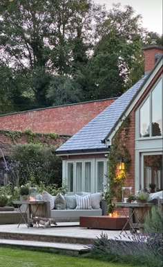 an outdoor patio with seating and fire pit in front of a brick building surrounded by greenery