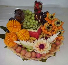 a platter filled with fruit and flowers on top of a white tablecloth covered table