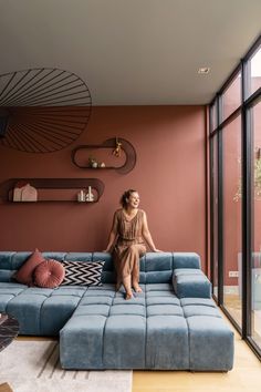 a woman sitting on top of a blue couch in a living room next to large windows