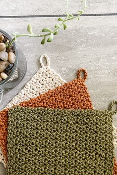 two crocheted potholders sitting on top of a table next to a plant