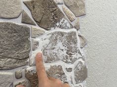 a hand pointing at a stone wall with water coming out of the cracks in it