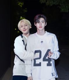 two young men standing next to each other in front of a dark background with trees