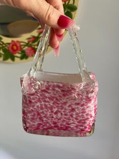 a hand holding a pink and white bag with clear handles, hanging from the ceiling