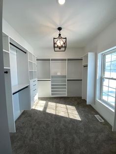 an empty walk - in closet with white cabinets and gray carpeted flooring is shown