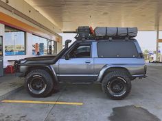 an suv with luggage strapped to the roof parked in a parking lot next to a gas station