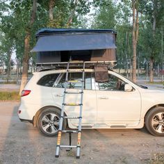 a white car parked in front of trees with a roof top tent attached to it