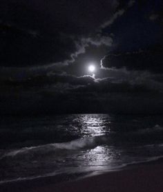 the moon is shining over the ocean on a cloudy night with waves crashing in front of it