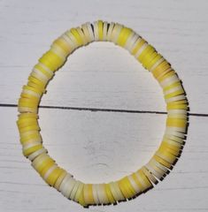 a yellow and white beaded bracelet on a wooden surface with a string attached to it