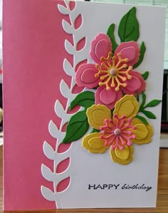 a pink and white birthday card with flowers on the front, sitting on a table