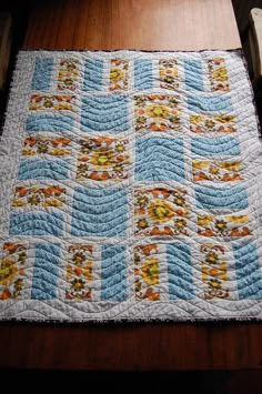 a quilted table runner on top of a wooden table with chairs in the background