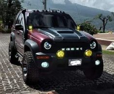 a red and black truck parked on top of a cobblestone road with mountains in the background