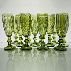 an assortment of green glass goblets sitting on a white table top in front of a gray background