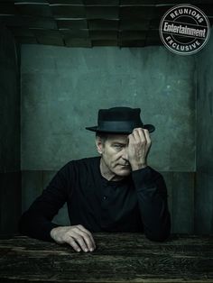 a man sitting at a table with his hands to his face and wearing a black hat