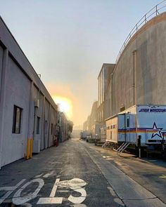 the sun is setting on an empty street in front of some storage buildings and trucks