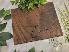 a wooden cutting board with the word family engraved on it next to flowers and greenery