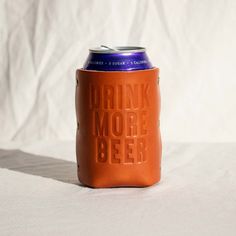 an orange leather can cooler with the words drink more beer on it, sitting on a white surface