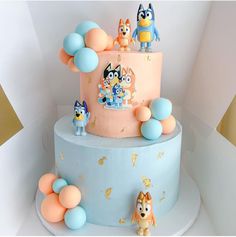 a blue and pink cake with cartoon characters on it's top, surrounded by balloons