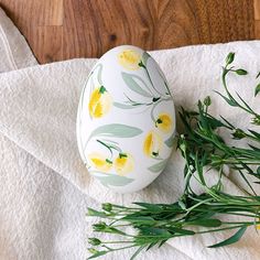 an egg with yellow flowers painted on it sitting next to some green leaves and white towels