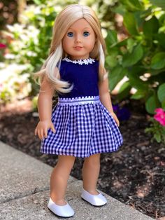 a doll with blonde hair wearing a blue dress and white shoes standing in front of flowers