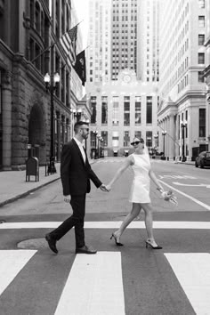 a man and woman walking across a crosswalk in the middle of a city holding hands