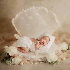 a newborn baby is sleeping in a white box surrounded by flowers and pearls on a beige background