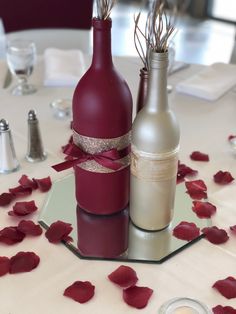 two wine bottles sitting on top of a table with rose petals in front of them